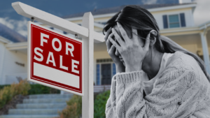 Woman holding her head in distress beside a large 'For Sale' sign outside a house yard.