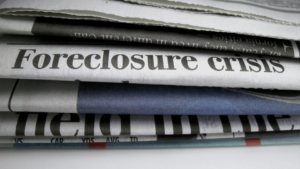 Newspaper front pages stacked, with a bold 'Foreclosure crisis' headline across the page