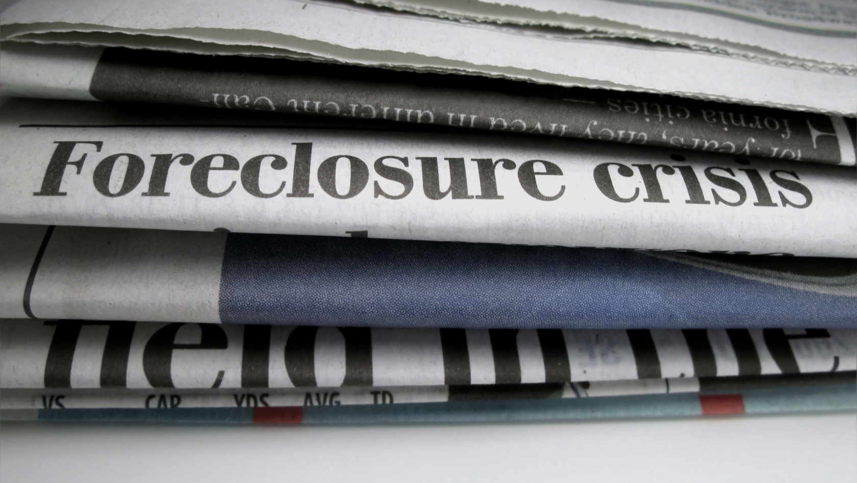 Newspaper front pages stacked, with a bold 'Foreclosure crisis' headline across the page