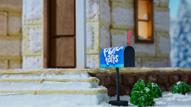 Blue curved-top mailbox on a black post with a red flag, set in a snowy front yard in front of a partially built house with yellow insulation.