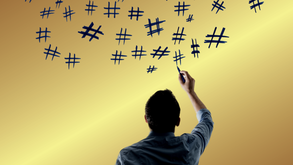 Person seen from behind writes blue hashtag symbols across a yellow gradient wall with a marker.
