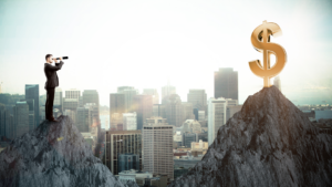 Businessman on a rocky peak aiming a telescope toward a giant golden dollar sign on another peak above a city skyline.