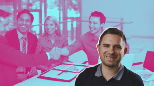 Smiling man in foreground with a group of colleagues shaking hands in the background, signaling a successful business partnership.
