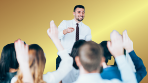 Speaker in a white shirt and striped tie high-fives a cheering crowd against a yellow gradient backdrop.