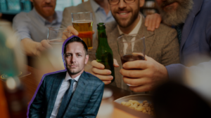 Group of friends toasting with drinks at a bar, with a cutout portrait of a man in a suit placed on the table in the foreground.