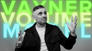 Black-and-white photo of a man gesturing with both hands, against a bright neon text backdrop.