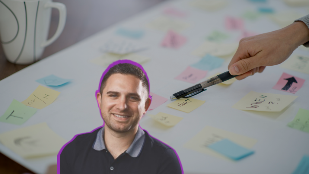 Smiling man cutout outlined in purple on a table covered with colorful sticky notes as someone writes with a marker nearby.