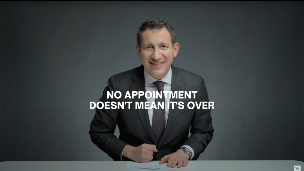 Smiling man in a dark suit sits at a desk, signing papers, with the bold caption: 'NO APPOINTMENT DOESN'T MEAN IT'S OVER' across the middle.