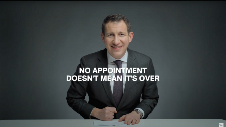 Smiling man in a dark suit sits at a desk, signing papers, with the bold caption: 'NO APPOINTMENT DOESN'T MEAN IT'S OVER' across the middle.