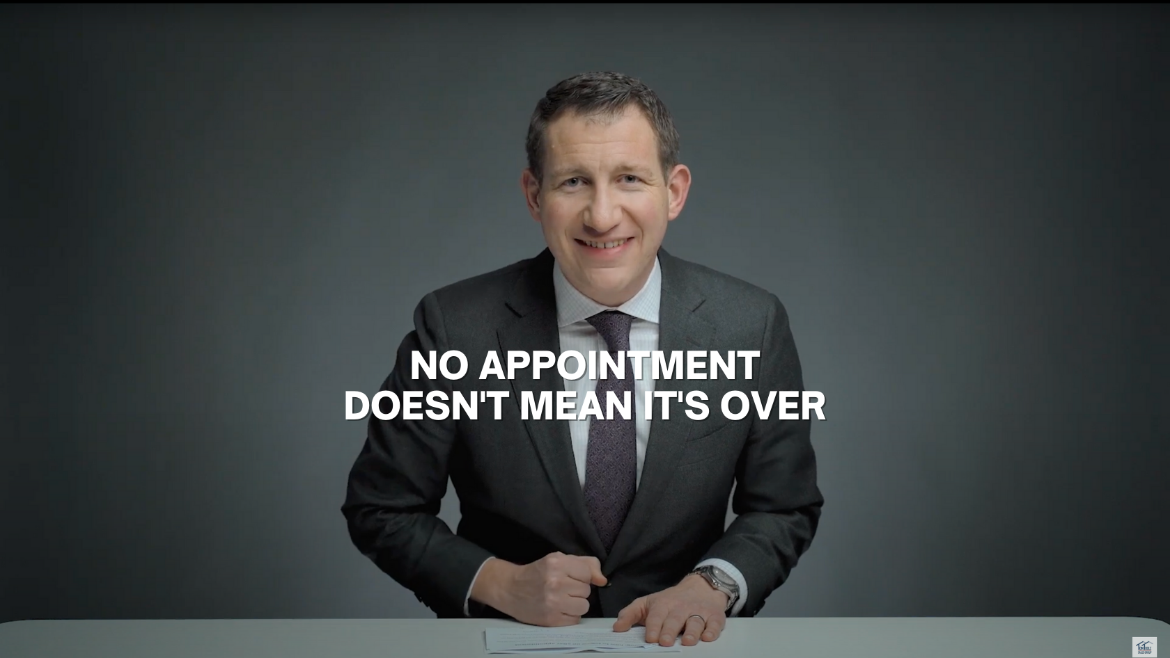 Smiling man in a dark suit sits at a desk, signing papers, with the bold caption: 'NO APPOINTMENT DOESN'T MEAN IT'S OVER' across the middle.