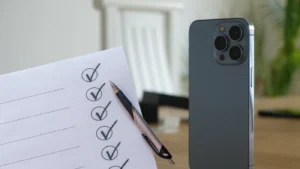 Checklist with checked boxes and a pen resting on a desk beside a modern smartphone on a wooden surface.