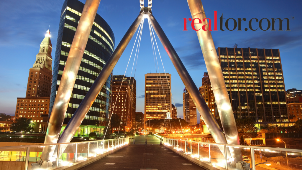 Evening city skyline with illuminated office buildings and a bridge, featuring the realtor.com logo in the top-right corner.