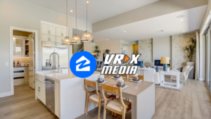 Open-concept kitchen and living room with white cabinets, island, and gray decor; VRX MEDIA logo centered over the scene.