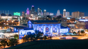 Nighttime cityscape with a blue-lit historic station in the foreground and a bright skyline behind.