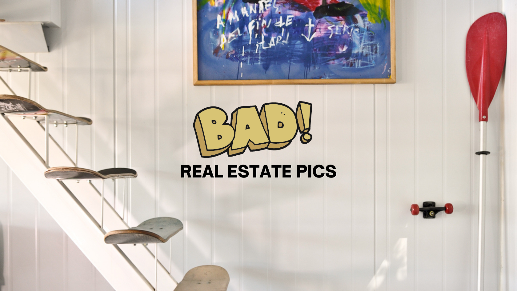 Humorous banner reading 'BAD!' with 'REAL ESTATE PICS' on a white paneled wall, framed art above, left staircase with skated steps, and a red paddle on the right.