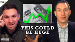 Two men sit at the edges of a dark set; in the center a close-up of a dollar with a bright green upward arrow, and bold text 'THIS COULD BE HUGE' across the bottom.