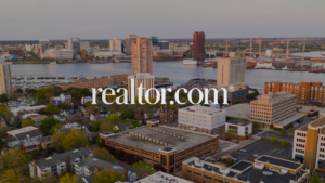 Aerial cityscape over a river with tall office buildings and a marina; realtor.com watermark across the center.