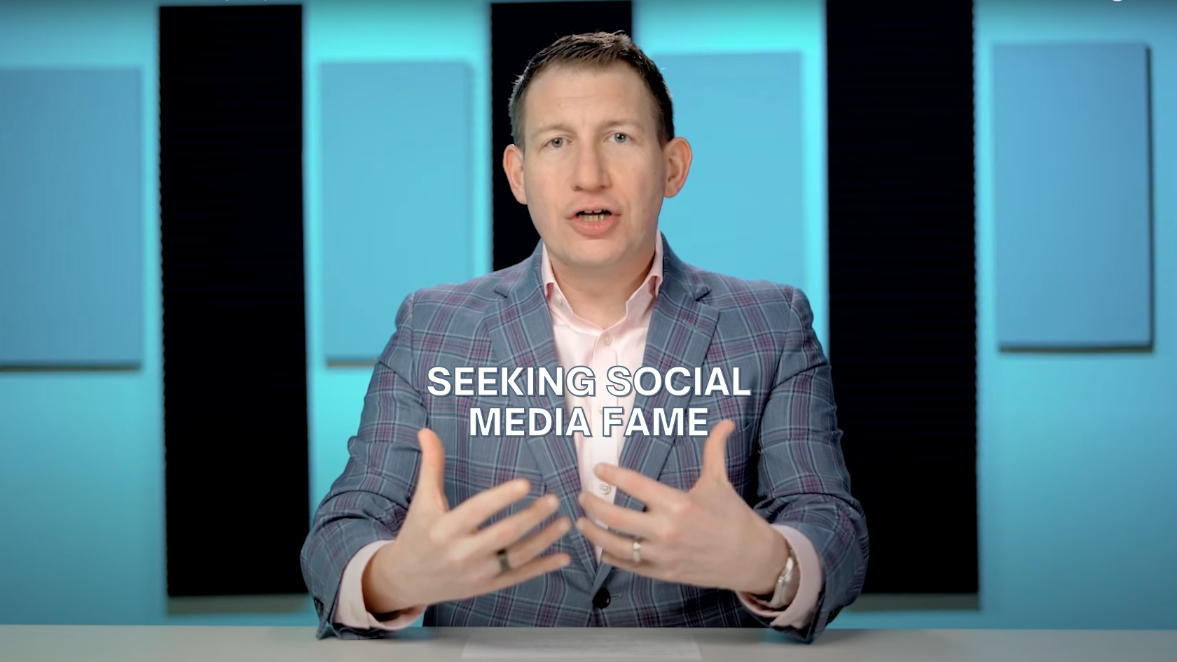 Presenter in a plaid blazer speaks at a desk, with the on-screen text 'SEEKING SOCIAL MEDIA FAME'.