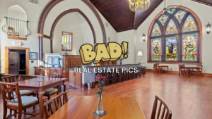 Interior of a large, church-like room with dark wood arches, stained-glass windows, and wooden tables; bold overlay reads 'BAD! REAL ESTATE PICS'.