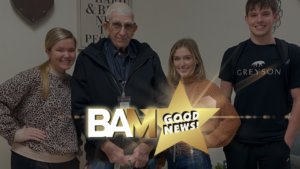 Four people posing for a group photo indoors, smiling; a large gold star with 'BAM Good News' overlays the lower center.