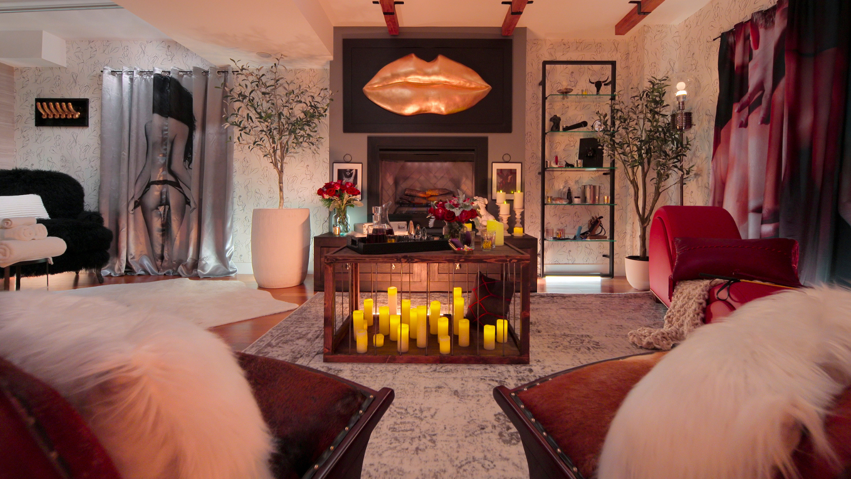 Lux lounge with candles on a central table and a copper lips sculpture above the fireplace, flanked by plants and shelves.