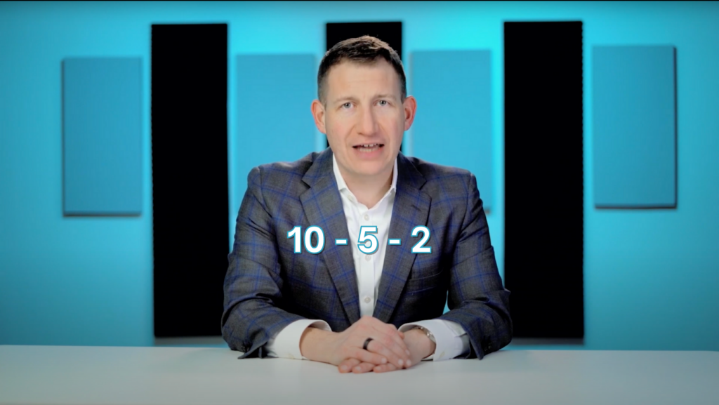 Male presenter in a blue checked blazer at a desk, with the math expression 10 − 5 − 2 on screen.