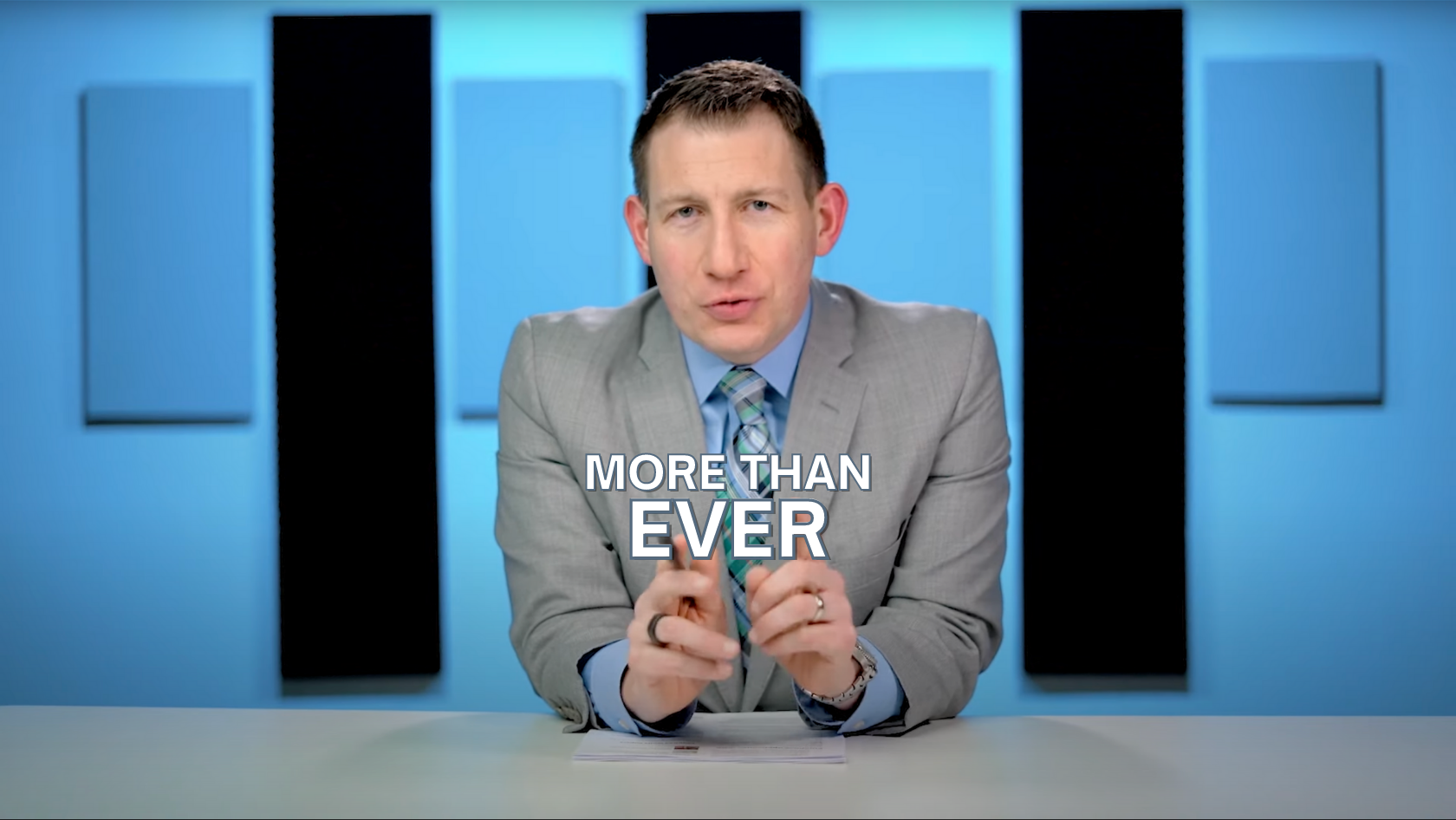 News anchor in a gray suit sits at a desk with a bold 'MORE THAN EVER' caption on screen in a blue-studio backdrop