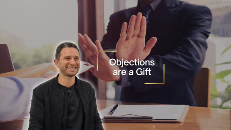 Smiling man in a black jacket at a desk; a suited colleague behind shows a stop gesture with hands, overlaid by 'Objections are a Gift'.