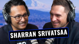 Two men wearing large over-ear headphones chat and smile during a podcast recording with microphones in front of them, a bold banner shows 'SHARRAN SRIVATSA' across the image.