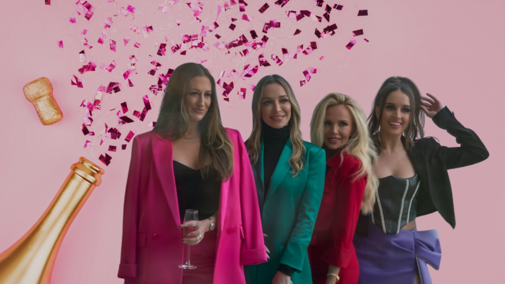 Four stylish women posing together at a party with pink background, champagne bottle and confetti above them.