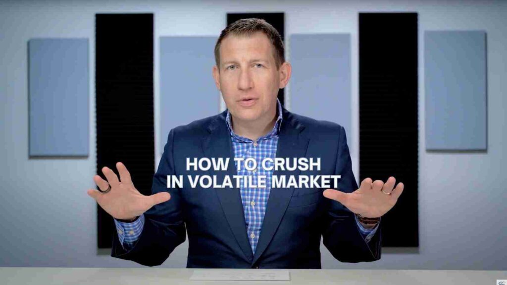 Host in a navy suit at a desk, hands extended, with the on-screen title 'HOW TO CRUSH IN VOLATILE MARKET' across the middle.