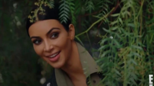 Smiling woman in a military camouflage jacket among green foliage outdoors.