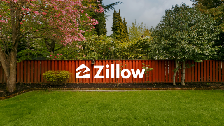 Zillow logo in white on a red wooden fence amid green shrubs and trees in a garden. The lawn is foregrounded.