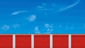 Row of red storage unit doors separated by white columns under a bright blue sky.