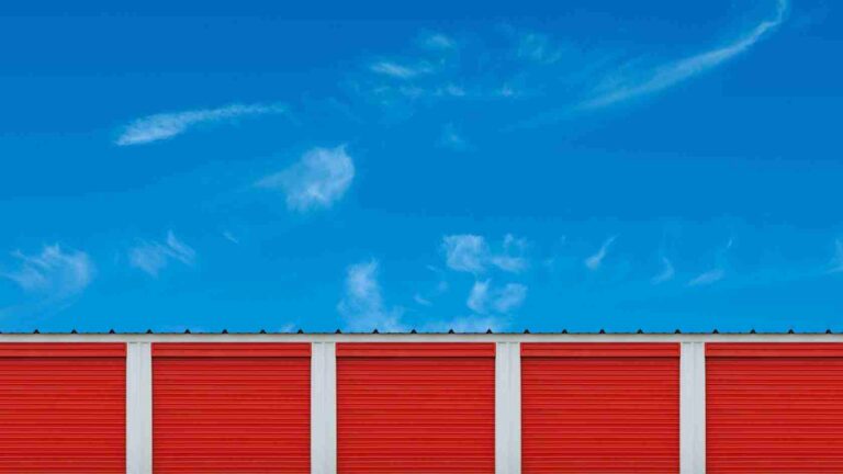 Row of red storage unit doors separated by white columns under a bright blue sky.