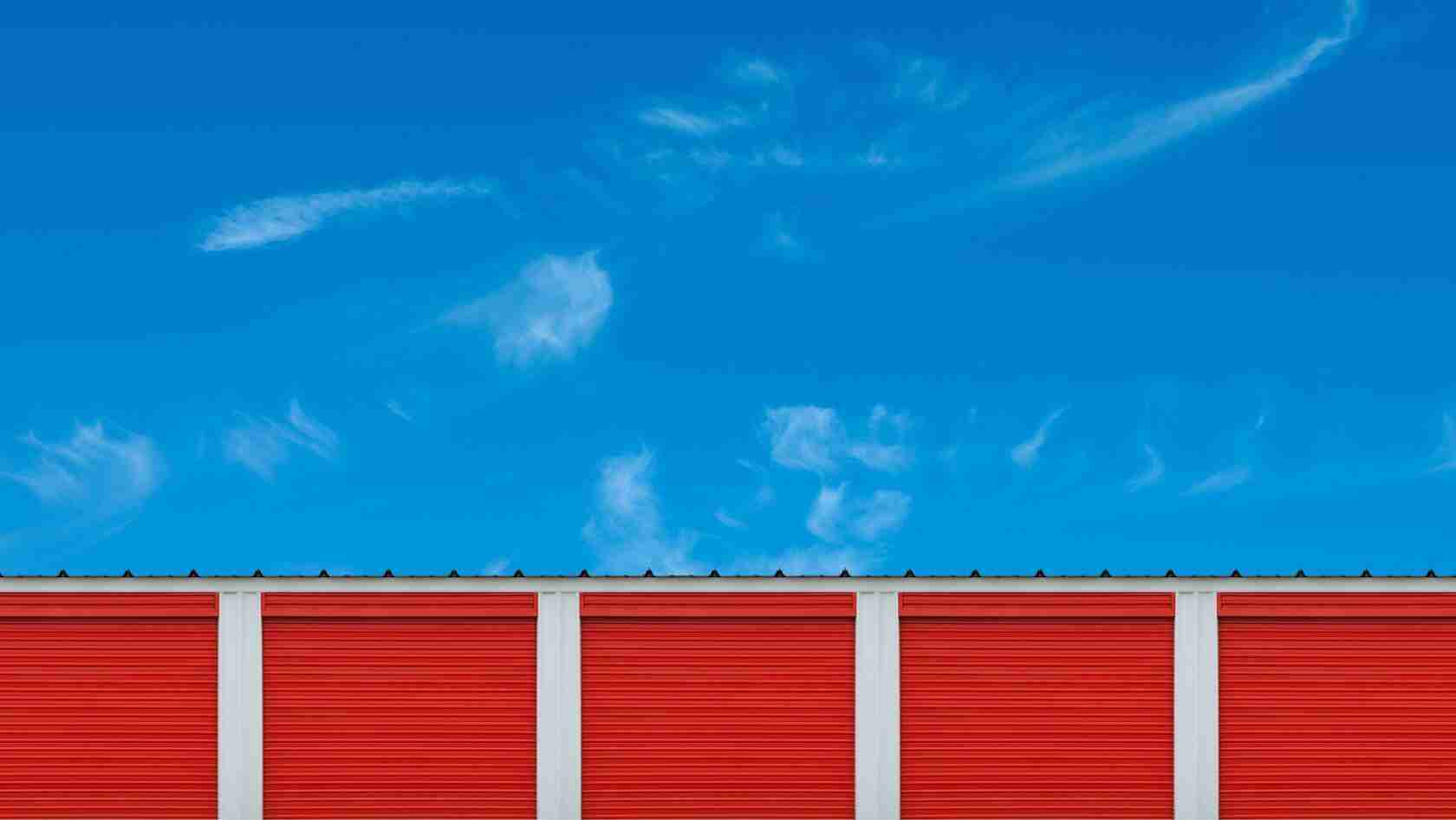 Row of red storage unit doors separated by white columns under a bright blue sky.