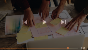 Team members collaborate on a design, arranging sticky notes and sketches on a wooden table with color swatches nearby