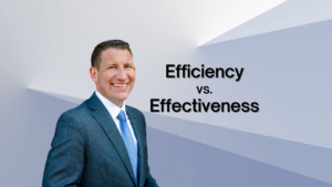 Smiling businessman in a blue suit on the left with bold text 'Efficiency vs. Effectiveness' on a geometric blue-gray background, representing a business topic cover.
