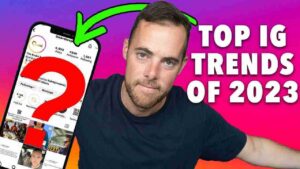 Presenter beside a tilted smartphone showing an Instagram page, with a large red question mark and a bold 'TOP IG TRENDS OF 2023' headline on a purple-to-orange gradient background.