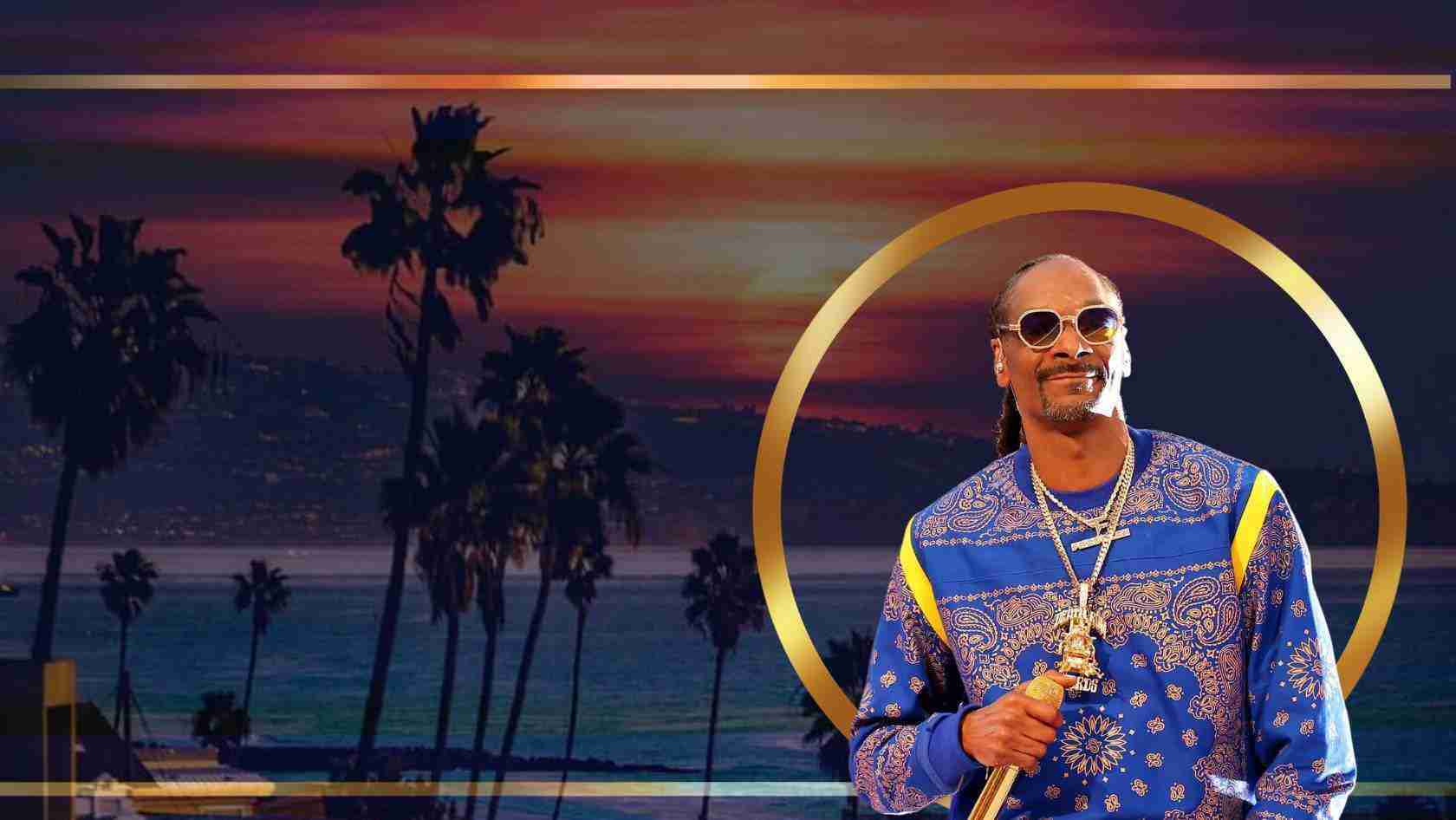Male performer in a blue patterned shirt with gold chains stands before a sunset beach backdrop with palm trees and a gold circular frame.