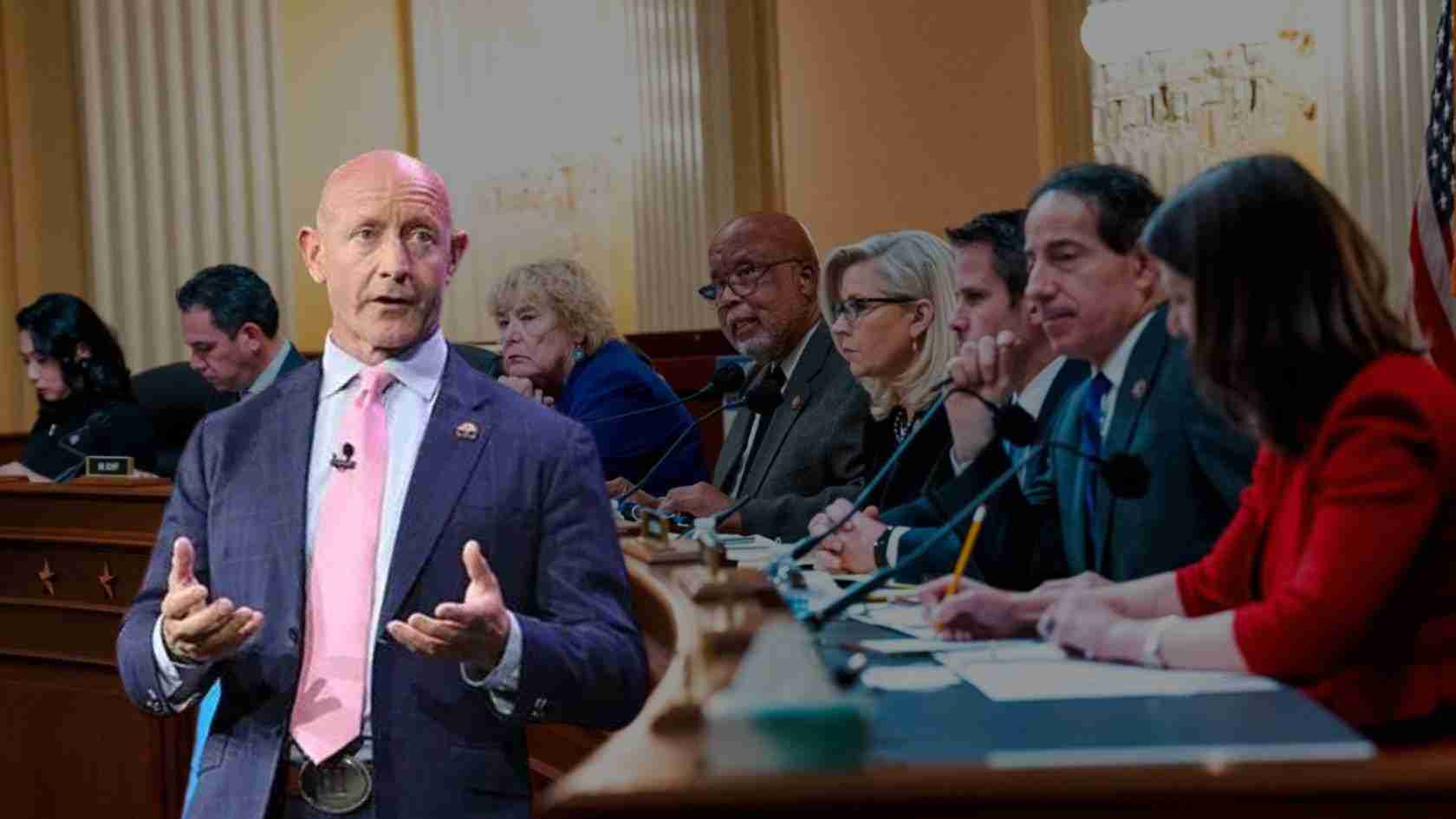Bald man in a navy suit and pink tie speaks passionately at a congressional hearing with panelists seated behind him at a long desk.