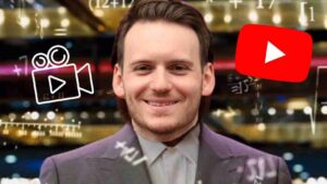 Smiling man in a suit on a studio backdrop with YouTube-style play icons overlay, suggesting video content about him.