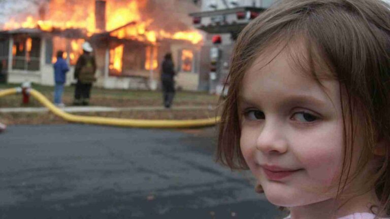 Young girl in foreground smiling with a burning building and firefighters behind her, a yellow fire hose on the ground.