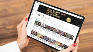 Person holding a tablet displaying a YouTube channel page titled Real Estate News Entertainment with video thumbnails aligned in rows.