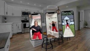 Three smartphone screens on stands display a woman exercising in a modern kitchen setting; outdoor house visible on the right.