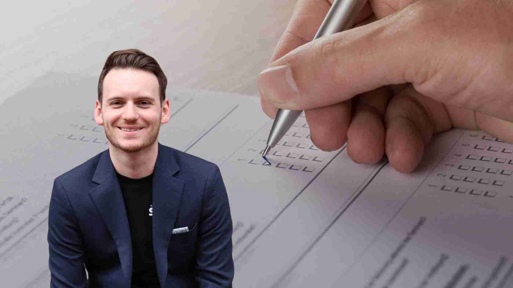 Smiling man in a navy blazer sits beside a close-up of a hand with a pen filling out a form with checkboxes.