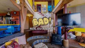 Bright, eclectic living space with blue seating, yellow walls, a fireplace, stairs, and a large TV, overlaid with a bold 'BAD!' cartoon and 'REAL ESTATE PICS' text.