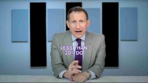 Presenter in a gray suit and purple tie sits at a desk, delivering a video briefing with the caption 'LESS THAN 20% DO' overlaid