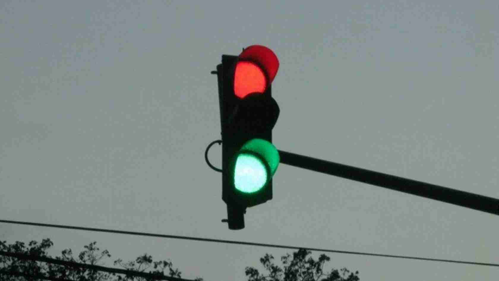 Traffic light with red and green signals visible on a pole against a gray sky.