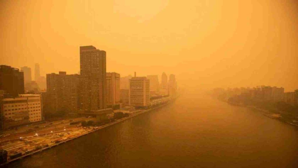 City skyline along a river under a thick orange haze (smog/sunset).